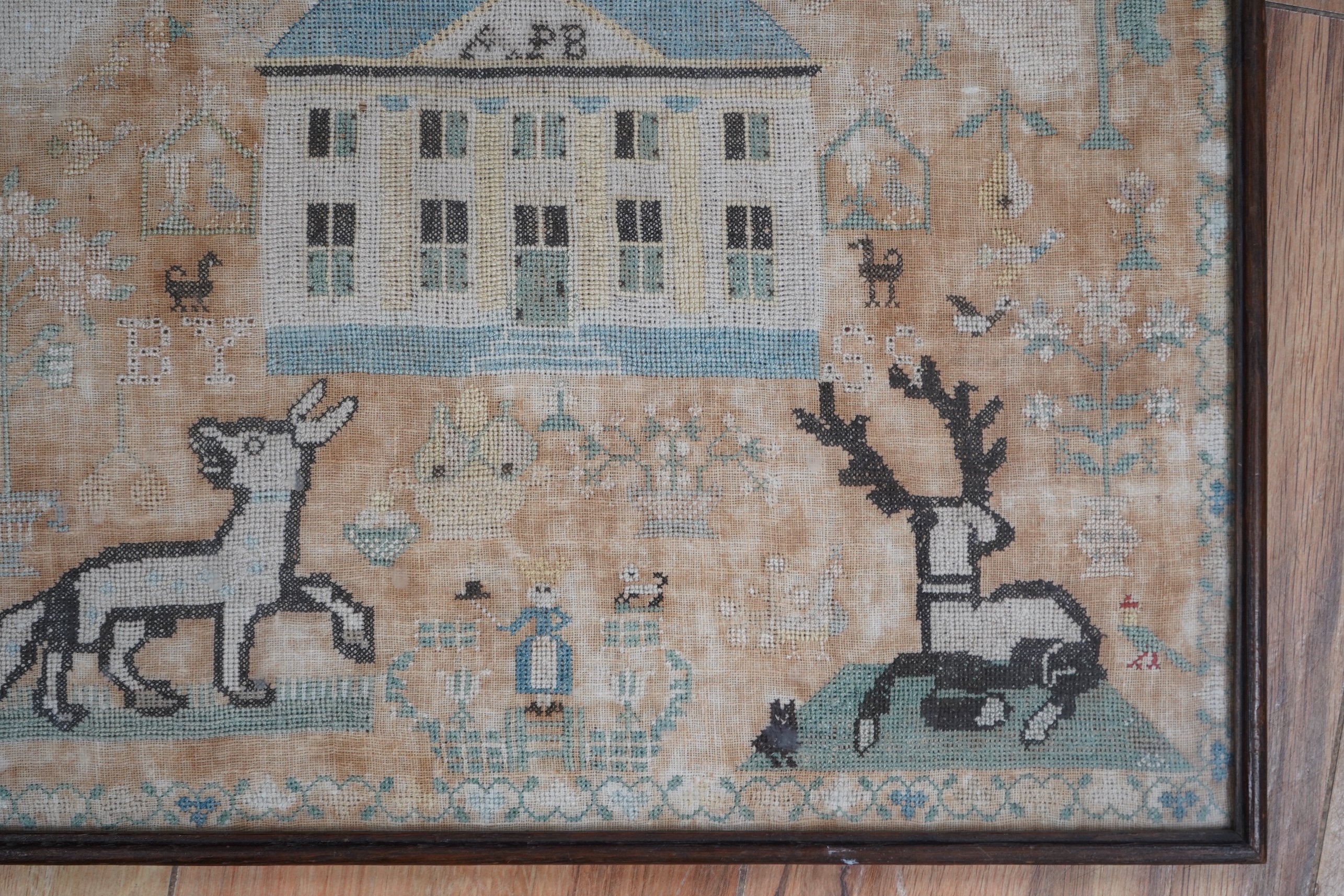 A framed 18th century sampler, dated 1779 by SS., worked in fine cross stitch with motifs of angels, figures, flowers, trees birds a fox and a stag surrounding a house with initials APB. 39cm x 37.5cm. Condition - the em